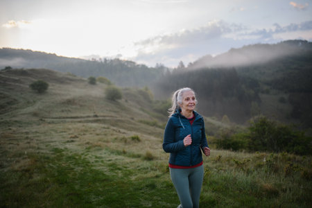 Senior woman jogging in nature on early morning with fog and mountains in background.の写真素材