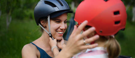 Young mother with little daughter preaparing for bike ride, putting on helmets.の写真素材