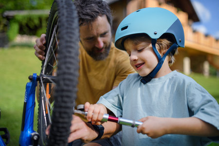 Father with little son together preparing bicycle for a ride, pumping up tyres in garden in front of house.の写真素材