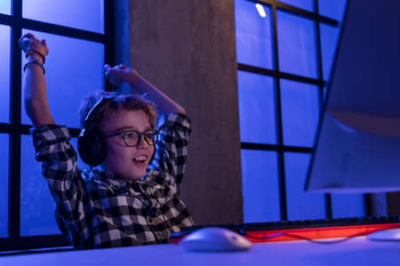 Young gamer boy with headphones playing computer video game.