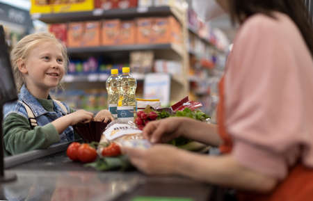 Close-up of little blond girl paying for grocery shopping in supermarket.の写真素材