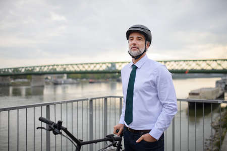 Businessman commuter on the way to work, standing on bridge and with bike, sustainable lifestyle concept.の写真素材