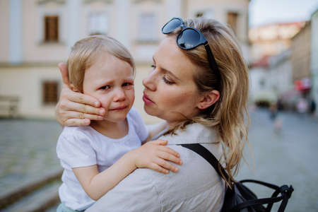 Mother consling her little daughter crying, holding her in arms in street in summer.の写真素材