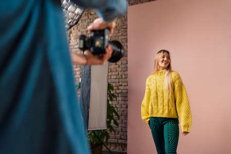 Young photographer taking picures of model, backstage of photoshooting in studio.