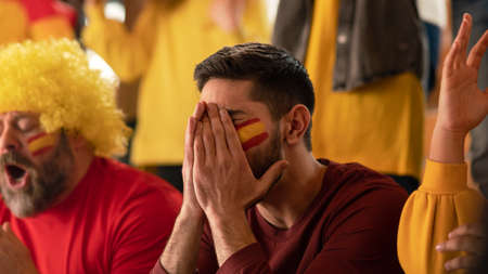 Worried football fans supporting spanish national team in live soccer match at stadium.の写真素材