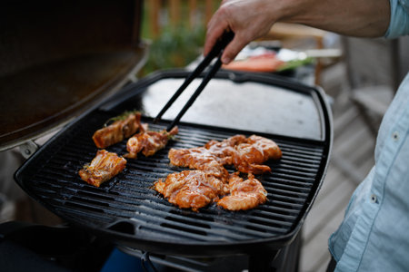 Unrecognizable man grilling meat, ribs and wings, on grill during family summer garden party, close-upの写真素材