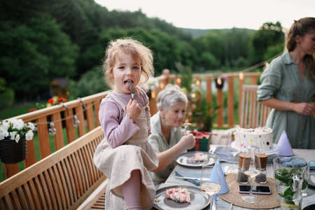 Little girl enjoying eating birthday cake during multi generation family celebration outside on patio.の写真素材