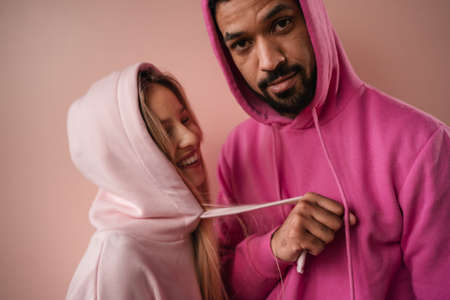 Fashion studio portrait of a happy young couple in hoodie posing over pink background.の写真素材
