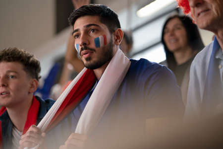 Worried football fans supproting French national team in live soccer match at stadium.