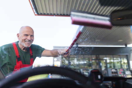 Senior worker washing car window at gas station.の写真素材