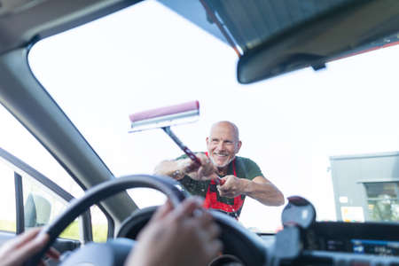 Senior worker washing car window at gas station.の写真素材