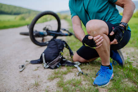 Active senior man in sportswear fell off bicycle on the ground and injured his knee, in park in summer.の写真素材