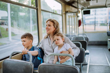 Young mother with little kids travelling in tram in summer, commuting and sustainable lifestyle concept.の写真素材