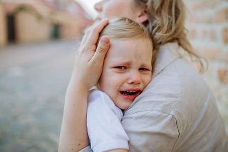 Unrecognizable mother consling her little daughter crying, holding her in arms in street in summer.の写真素材