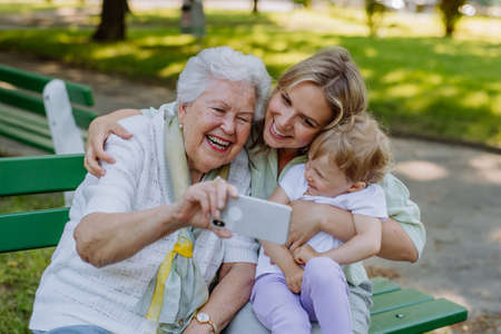 Great grandmother taking selfie with her granddaughter and kid when sitting in park in summer.