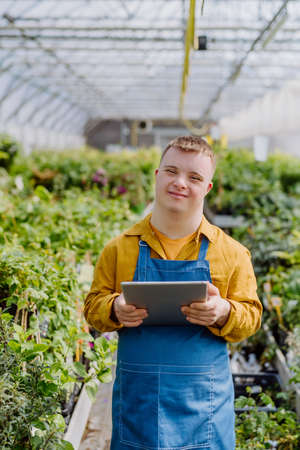 Young man with Down syndrome working in garden centre, holidng clipboard and checking plants.の写真素材