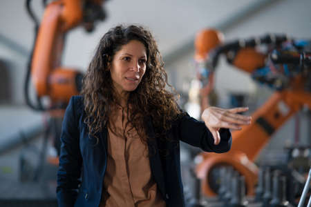 Automation female engineer talking to somebody about programming robotic arm in factory.