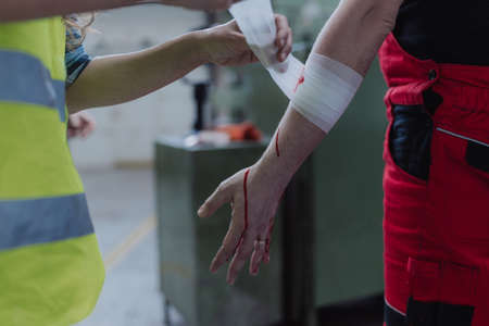 Woman is helping her colleague after accident in factory. First aid support on workplace concept.