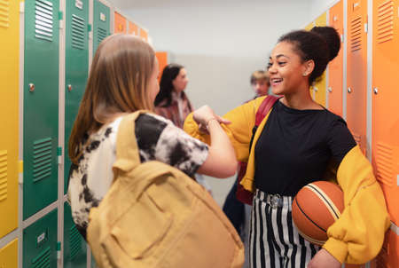 Young high school students meeting and greeting near locker in campus hallway talking and high...