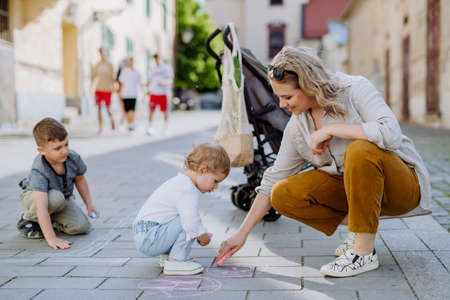 Little children with mother drwing with chalks on sidewalk in city on summer sunny day. Creative development of children.の写真素材