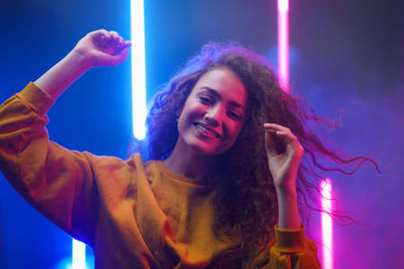 Portrait of a happy young woman dancing over neon light background at disco party