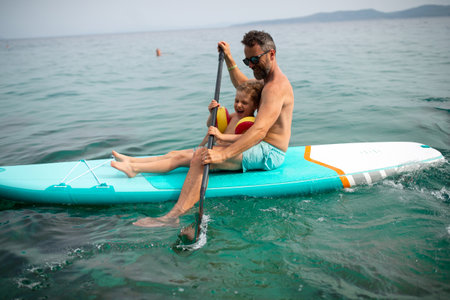 Happy father and little son on paddle board in sea together. Fatherhood and quality time with child concept.の写真素材