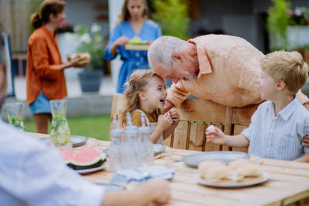 Multi generation family having garden party celebration, grandfather is entertaining grandchildren, laughing and having fun.の写真素材