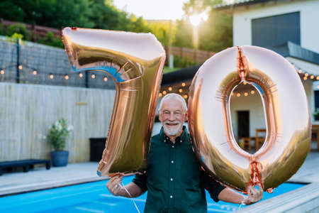 Man with number 70 balloons celebrating birthday near backyard pool.の写真素材