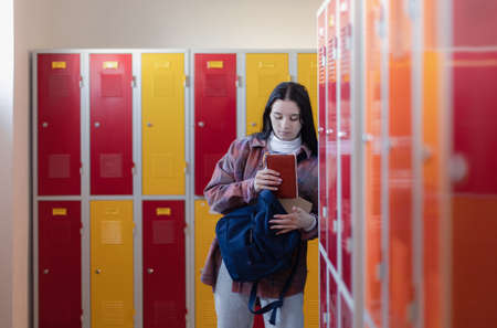 Sad teenage student standing in corridor near colorful lockers and packing book to backpack in campus hallway, back to school concept.の写真素材