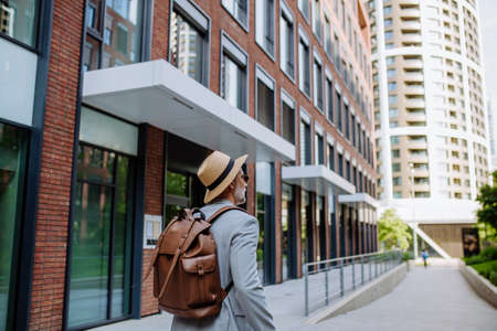 Rear view of man wearing straw hat and backpack walking in street, businessman in casual clothes in summer on the way to work.の写真素材