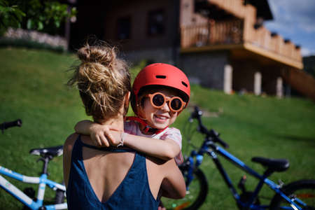 Young mother with little daughter preaparing for bike ride, putting on helmets and hugging.の写真素材