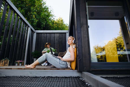 Happy young couple with laptop resting outdoors in a tiny house, weekend away and remote office...