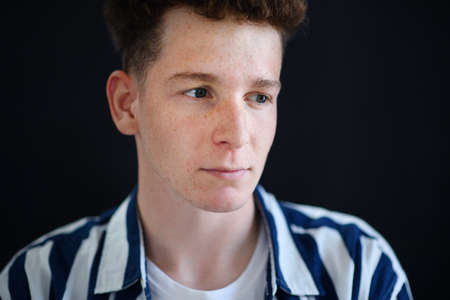 Portrait of thoughtful handsome young man with ginger hair and freckles looking away on black...