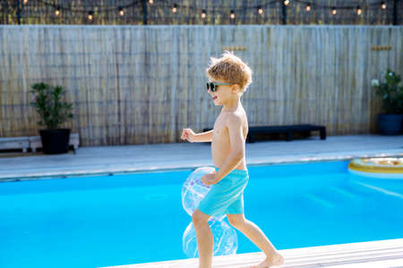 Happy kid having fun when running round the swimming pool with. Summer outdoor water activity for...
