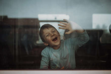 Happy little boy waving through window to say goodbye when travelling in train.の写真素材