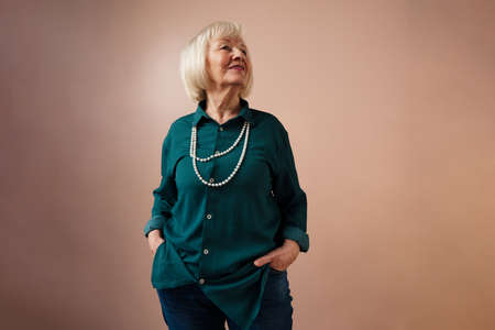 Smiling elegant elderly woman on pink color background, studio portrait
