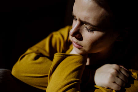 Woman suffering from depression and lying on floor with her hands covering head on black background.