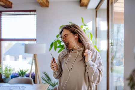 Happy young woman with earphones dancing, enjoying leisure weekend at home, stress free conceptの写真素材