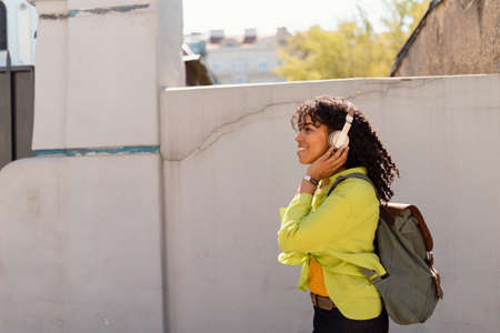 Young biracial woman wearing headphones and enjoying listening to music outdoors in street.