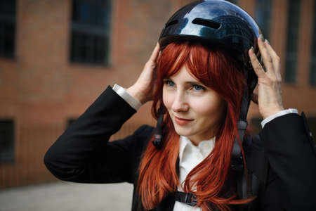 Portrait of businesswoman commuter on the way to work putting on cycling helmet, sustainable...