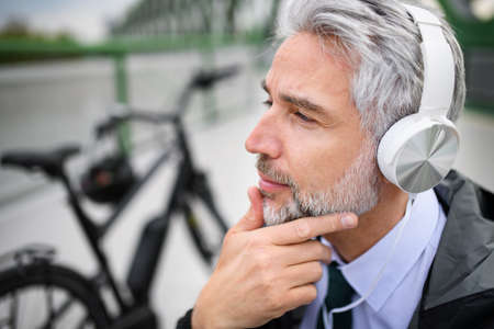 Businessman with bike sitting on bench, listening to music and resting. Commuting and alternative transport conceptの写真素材