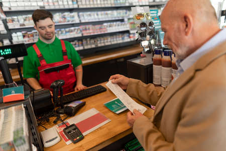 Cheerful young Down Syndrome employee giving bill to costumer in gas station cafe.の写真素材