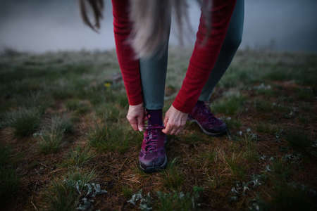 Close-up of senior woman tying her shoelaces before exercise in nature on early morning with fog.の写真素材