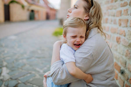 Mother consling her little daughter crying, holding her in arms in street in summer.の写真素材