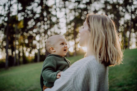 Mother holding her little baby son wearing knitted sweater during walk in nature, close-upの写真素材