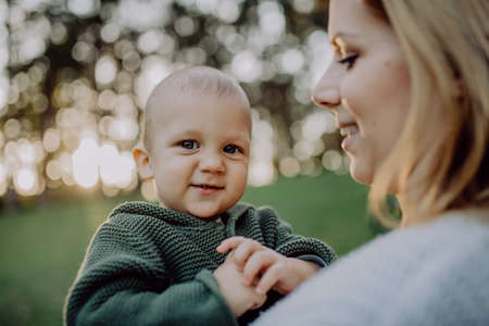 Mother holding her little baby son wearing knitted sweater during walk in nature, close-upの写真素材
