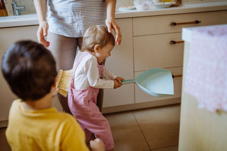Little boy and girl helping to clean house using pan and brush as they sweep up dirt off floor.の写真素材