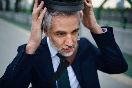 Portrait of businessman commuter on the way to work putting on cycling helmet, sustainable lifestyle...