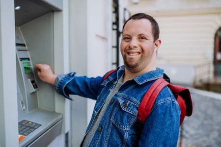 Happy young man with Down sydrome using a street ATM machine and withdrawing money.の写真素材