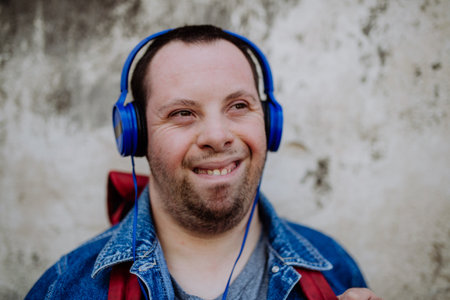 Close-up portrait of happy young man with Down sydrome listening to music when walking in street.の写真素材